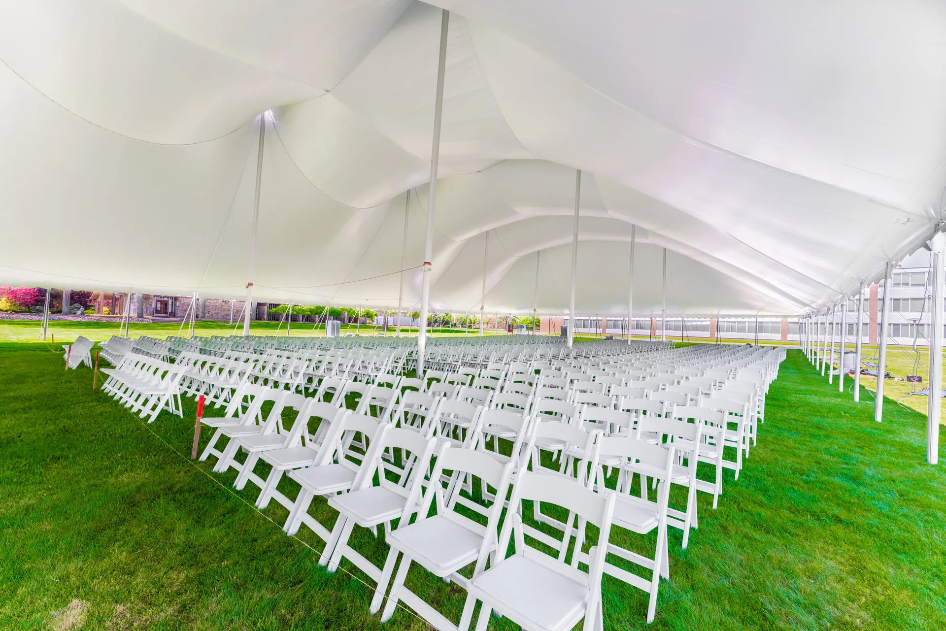 Rows of white chairs installed under a high tension fabric tent before a ceremony